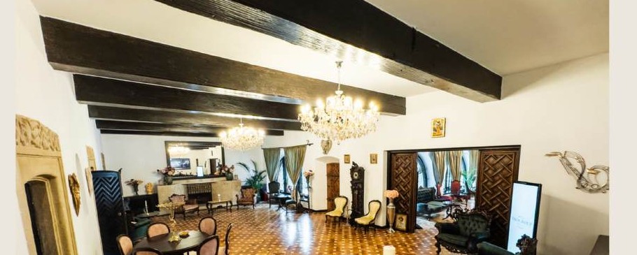 Salonul interbelic al vilei, cu grinzi aparente de lemn, două candelabre de cristal, șemineu și mobilier de epocă